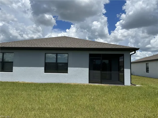 Rear view of house featuring a lawn, roof with shingles, a sunroom, and stucco siding