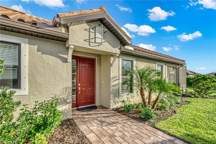 Stucco exterior featuring a red entry door, decorative outdoor lighting, and a paved brick walkway