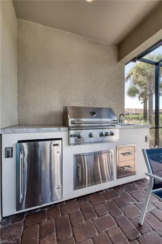 Outdoor kitchen featuring a built-in stainless steel grill, integrated refrigerator, and ample counter space with a sink