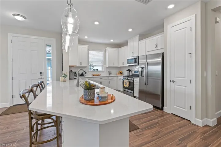 Open-concept kitchen featuring a spacious island with a light-toned countertop, white cabinetry, stainless steel appliances, and wood-finish flooring