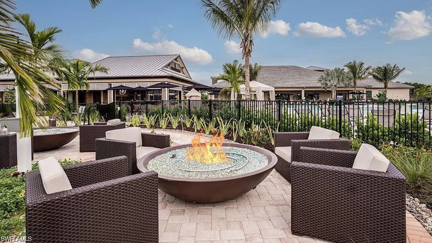 Outdoor patio featuring a built-in fire pit with decorative glass, paver flooring, and lush perimeter landscaping