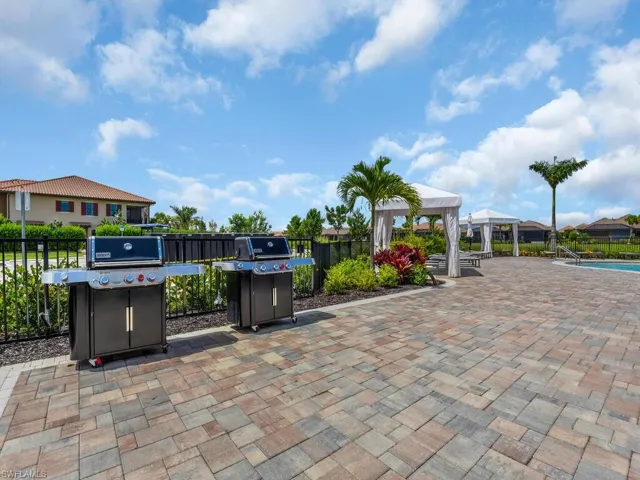 Paver patio featuring two built-in grills, bordered by mature landscaping and a black metal fence