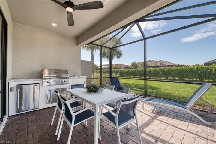 Screened lanai featuring a built-in outdoor kitchen with stainless steel appliances and a stone-finish countertop