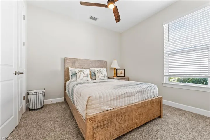 Bedroom featuring neutral wall tones, textured carpet, a ceiling fan with integrated lighting, a window with horizontal blinds, and a solid core door