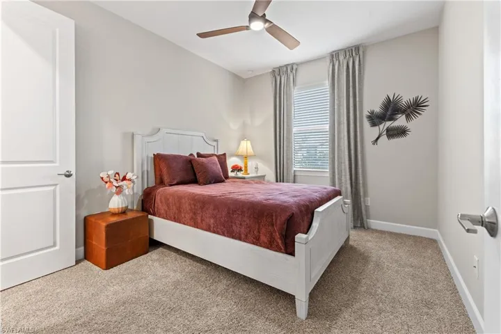 Carpeted bedroom featuring a ceiling fan with light fixture, window with blinds and drapes, and a white paneled door