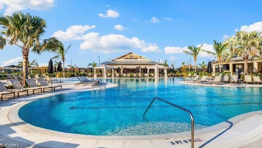 Expansive resort-style pool featuring a curvilinear design, surrounding lounge areas, multiple entry points, and a distant amenity building with covered outdoor seating