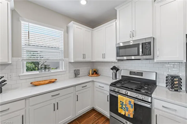 Kitchen featuring white shaker cabinetry, light-toned countertops, a subway tile backsplash, stainless steel appliances, and wood-finish flooring