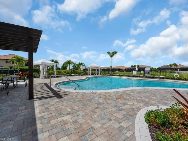 Expansive outdoor pool area featuring a freeform swimming pool, paver deck, multiple cabanas, and a pergola-covered dining space