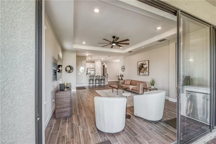 Indoor-outdoor living space featuring wood-finish flooring, a tray ceiling with recessed lighting, and a dark-toned ceiling fan