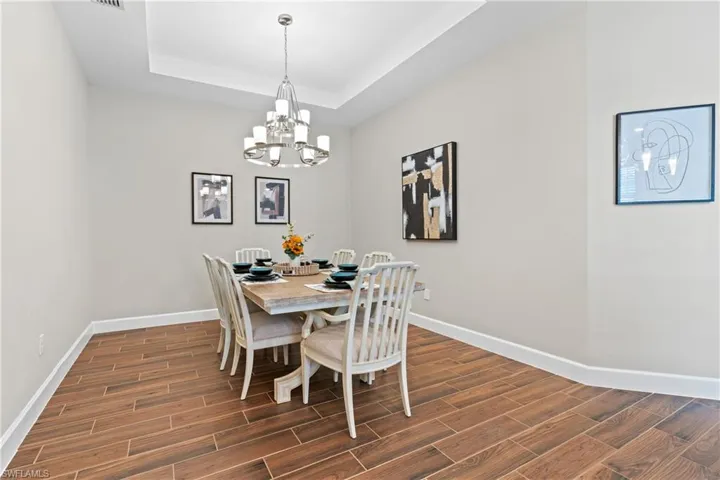 Dining area featuring wood-finish flooring, a contemporary chandelier, a tray ceiling, and white baseboards