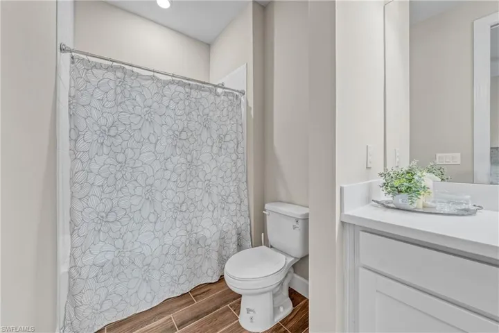Bathroom featuring wood-finish tile flooring, a white vanity with a light-toned countertop, a shower with a chrome shower rod, a white toilet, and neutral wall paint