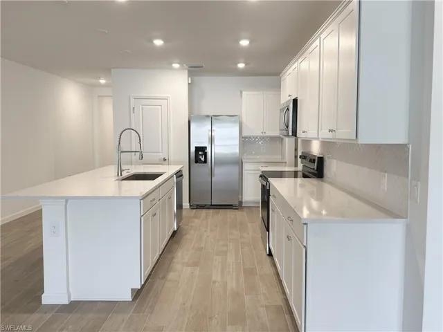 Kitchen featuring stainless steel appliances, white cabinetry, light stone countertops, light wood-style flooring, and backsplash