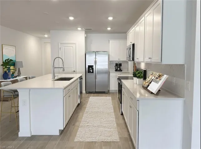 Virtually staged kitchen featuring stainless steel appliances, white cabinetry, light stone countertops, light wood-style flooring, and backsplash