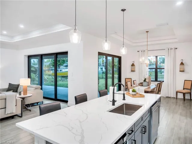 Kitchen with a raised ceiling, light wood finished floors, open floor plan, light stone countertops, and a kitchen island with sink