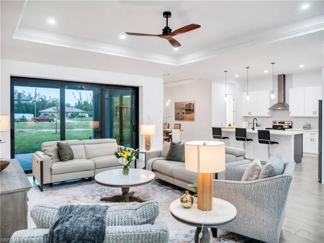 Living area featuring ceiling fan, light wood finished floors, a raised ceiling, ornamental molding, and recessed lighting