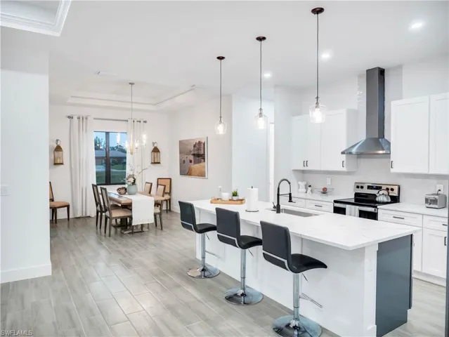 Kitchen with stainless steel electric stove, white cabinets, a breakfast bar area, light stone counters, and a raised ceiling