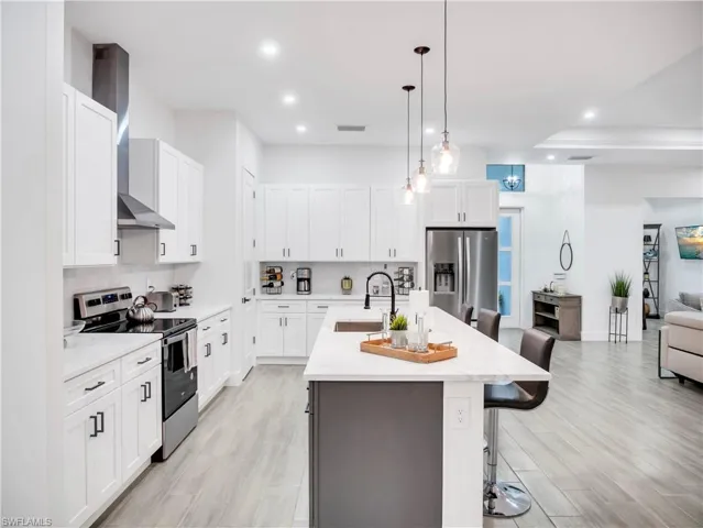 Dual tone kitchen with stainless steel appliances, a breakfast bar, light stone counters, a center island with sink, and open floor plan