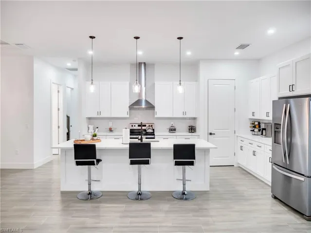 Kitchen with stainless steel appliances, a breakfast bar area, white cabinets, pendant lighting, and a kitchen island with sink