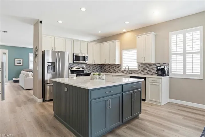 Two tone kitchen with two tone cabinetry, stainless steel appliances, light stone countertops, a kitchen island, and light wood-style flooring