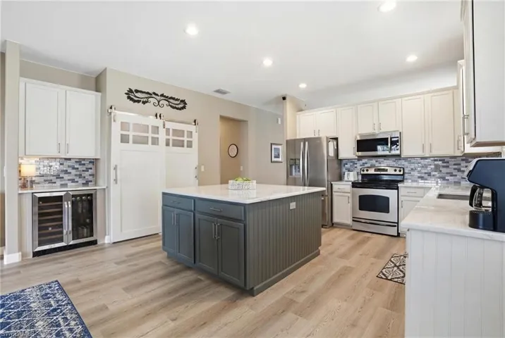 Dual tone kitchen featuring decorative backsplash, two tone cabinets, stainless steel appliances, beverage cooler, and light stone counters