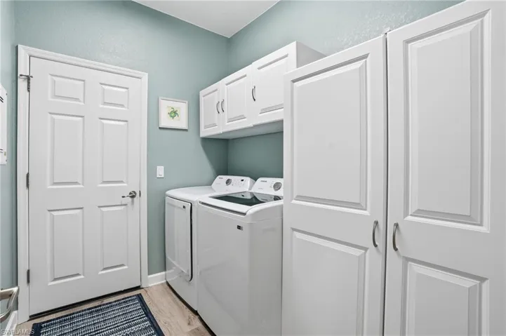 Laundry area featuring cabinet space, washing machine and clothes dryer, light wood-style floors, and a textured wall