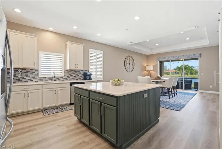Kitchen featuring two tone cabinetry, a center island, backsplash, light wood-style floors, and stainless steel appliances
