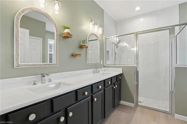 Bathroom featuring a shower stall, double vanity, light wood-type flooring, and recessed lighting