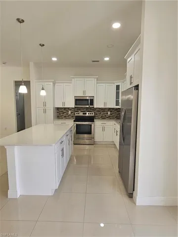 Kitchen with white cabinetry, stainless steel range oven, light tile patterned floors, white refrigerator, and a kitchen island