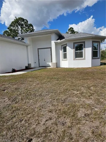 View of front facade with a front lawn, stucco siding, and roof with shingles