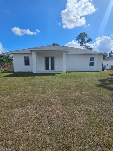 Rear view of property with stucco siding, a lawn, and roof with shingles