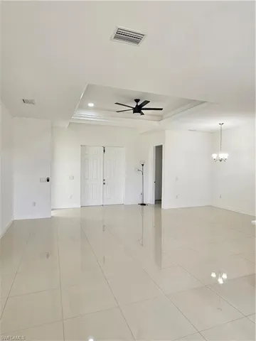 Unfurnished room with a raised ceiling, ceiling fan, hanging lights, and light tile patterned floors