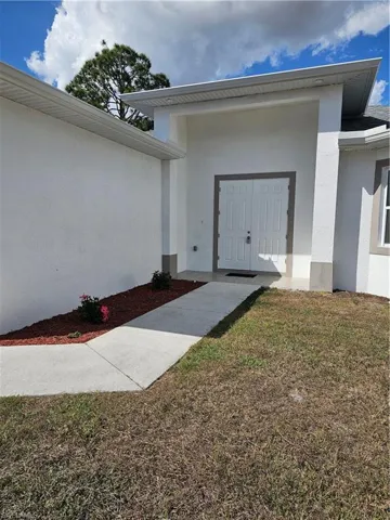 Entrance to property with stucco siding and a lawn