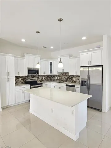 Kitchen featuring light stone countertops, refrigerator, range, a kitchen island, and tasteful backsplash