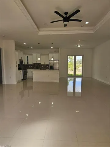 Unfurnished living room featuring ceiling fan, a tray ceiling, recessed lighting, ornamental molding, and light tile patterned floors