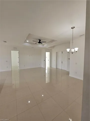 Spare room with a raised ceiling, ceiling fan, a chandelier, and light tile patterned flooring