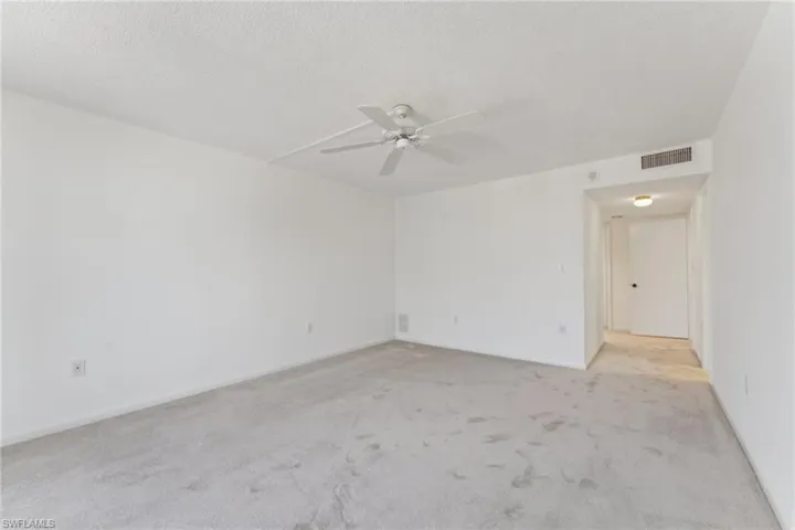 Spare room featuring a textured ceiling, baseboards, light colored carpet, visible vents, and ceiling fan