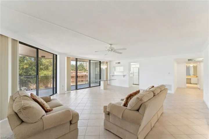 Living area featuring light tile patterned flooring, expansive windows, ceiling fan, and visible vents