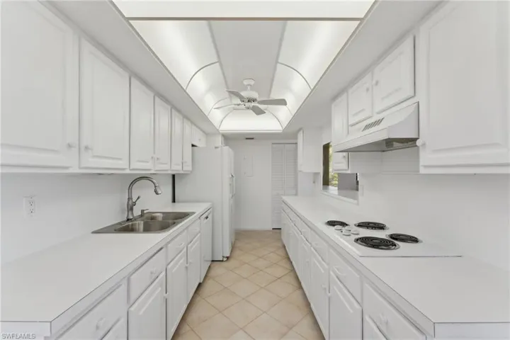 Kitchen with white cabinets, white appliances, a ceiling fan, under cabinet range hood, and a sink