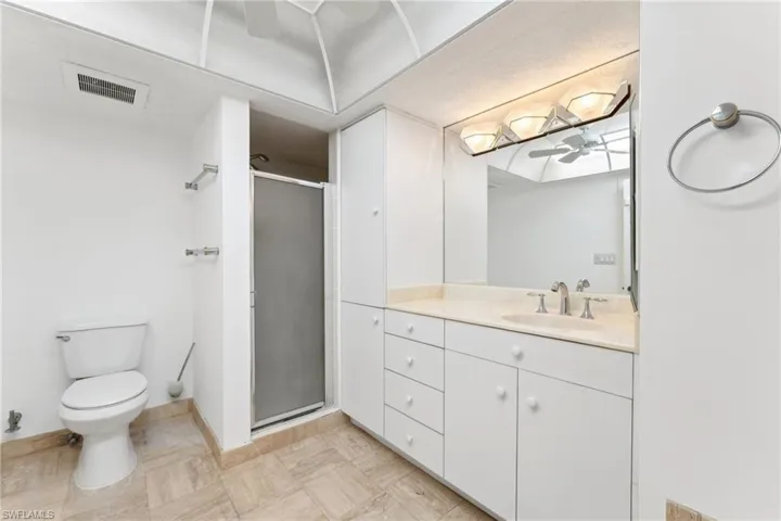 Bathroom with vanity, toilet, a stall shower, ceiling fan, and visible vents
