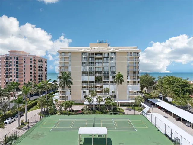View of tennis court featuring a water view and fence