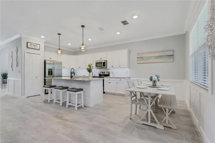 Kitchen with a breakfast bar, a kitchen island with sink, white cabinetry, crown molding, and decorative light fixtures