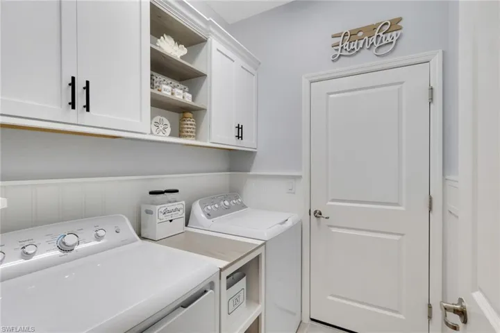Laundry area with wainscoting, a decorative wall, washing machine and clothes dryer, and cabinet space