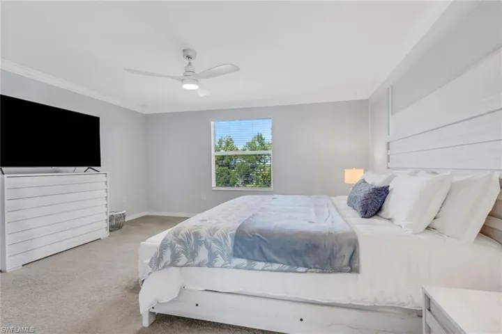 Carpeted bedroom with a ceiling fan and ornamental molding