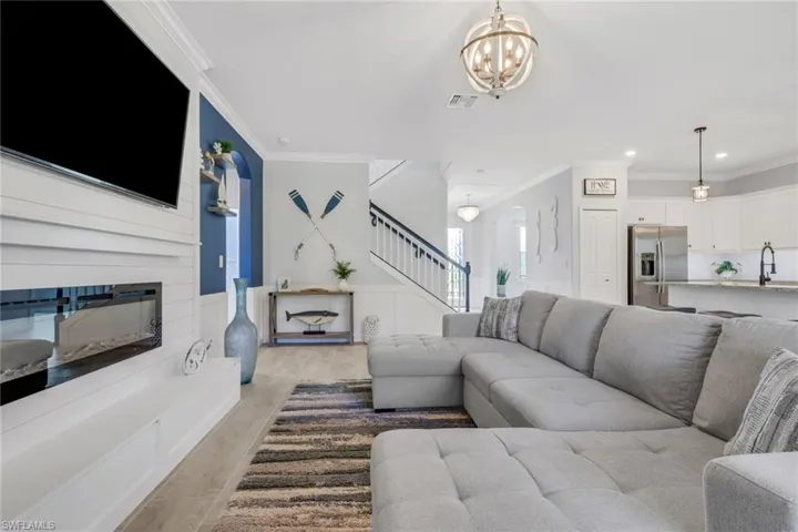 Living room featuring a large fireplace, ornamental molding, wainscoting, light wood finished floors, and suspended lighting