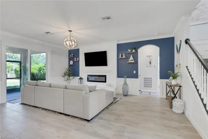 Living room featuring arched walkways, wainscoting, ornamental molding, a chandelier, and a fireplace