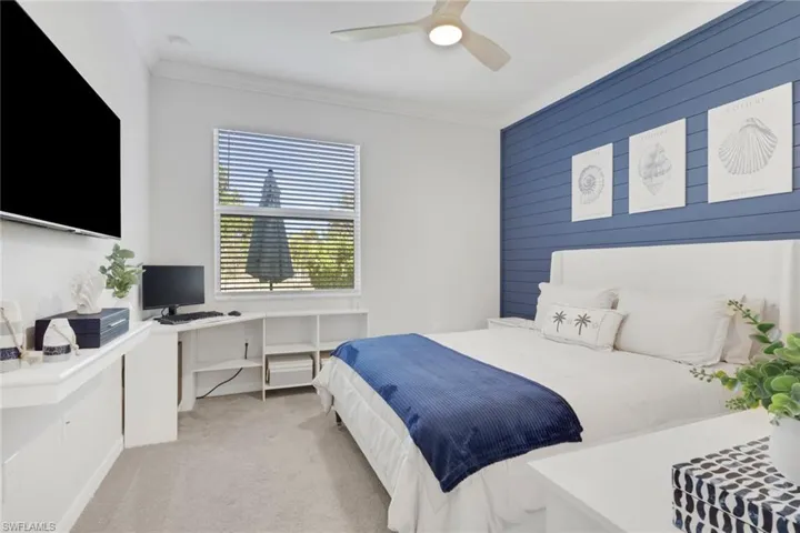 Bedroom with light carpet, a ceiling fan, wooden walls, a desk, and an accent wall