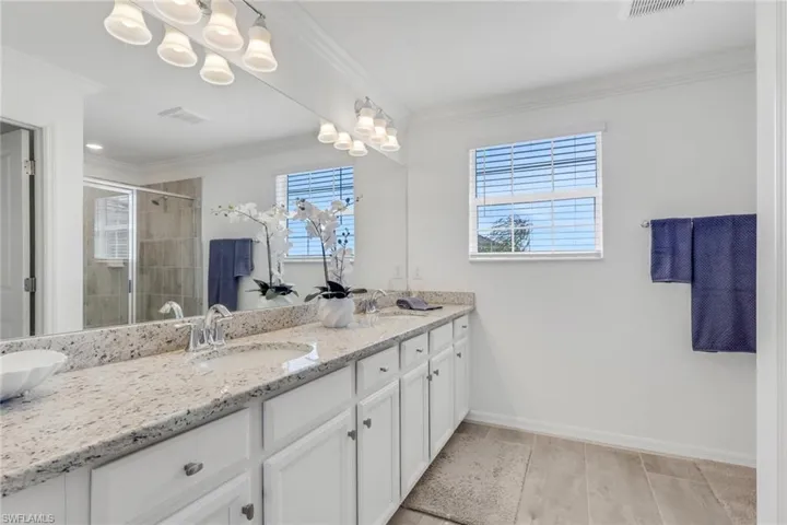Bathroom featuring double vanity, a shower stall, ornamental molding, suspended lighting, and wood tiled floors
