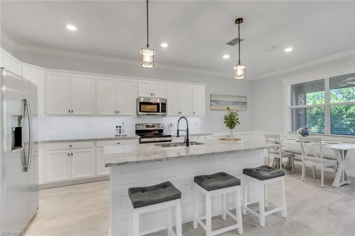 Kitchen with stainless steel appliances, white cabinetry, light stone countertops, a breakfast bar area, and crown molding