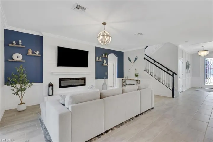 Living room with suspended lighting, a wainscoted wall, wood finish floors, a fireplace, and arched walkways