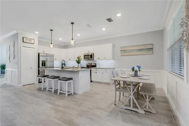 Kitchen featuring a wainscoted wall, a breakfast bar, white cabinetry, a center island with sink, and ornamental molding